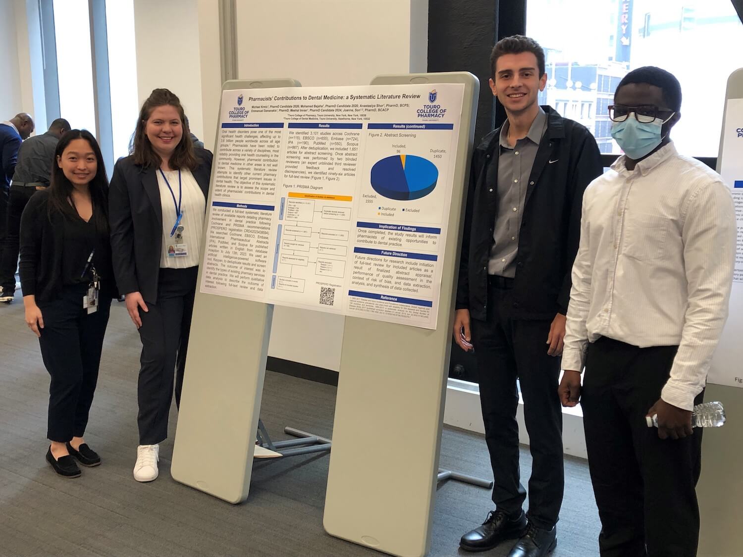 Four Touro College of Pharmacy students stand by a placard describing a research study.