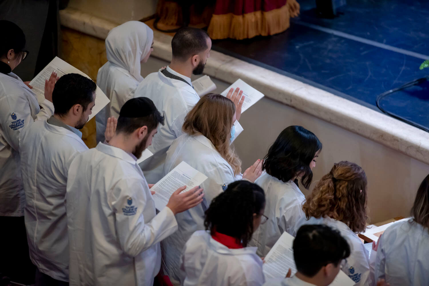 Pharmacy students in white coats reciting the Pharmacist Oath.