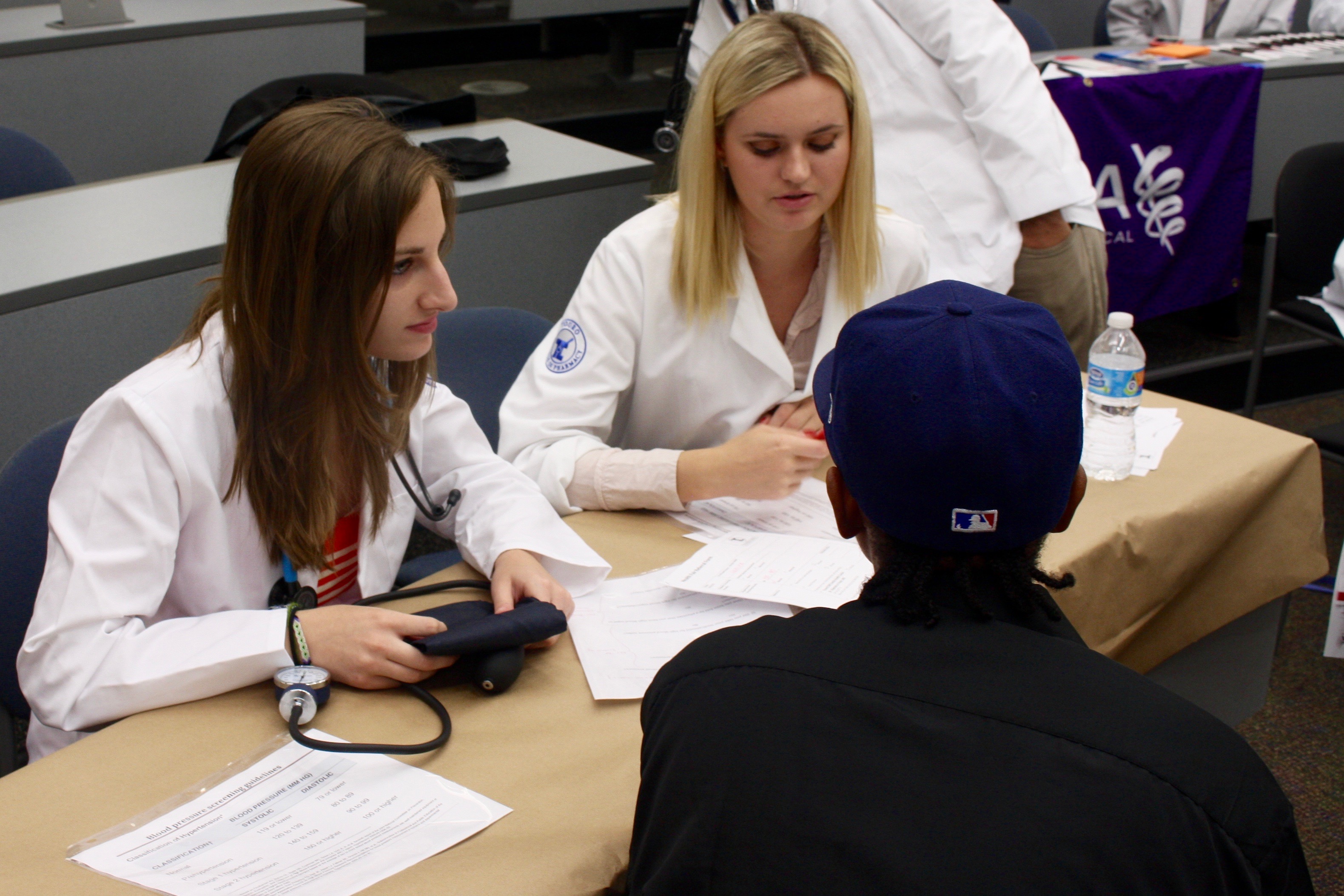 A TouroCOM D.O. student and a TCOP pharmacy student take a visitor's blood pressure during the TouroCOM-TCOP Fall Health Fair.