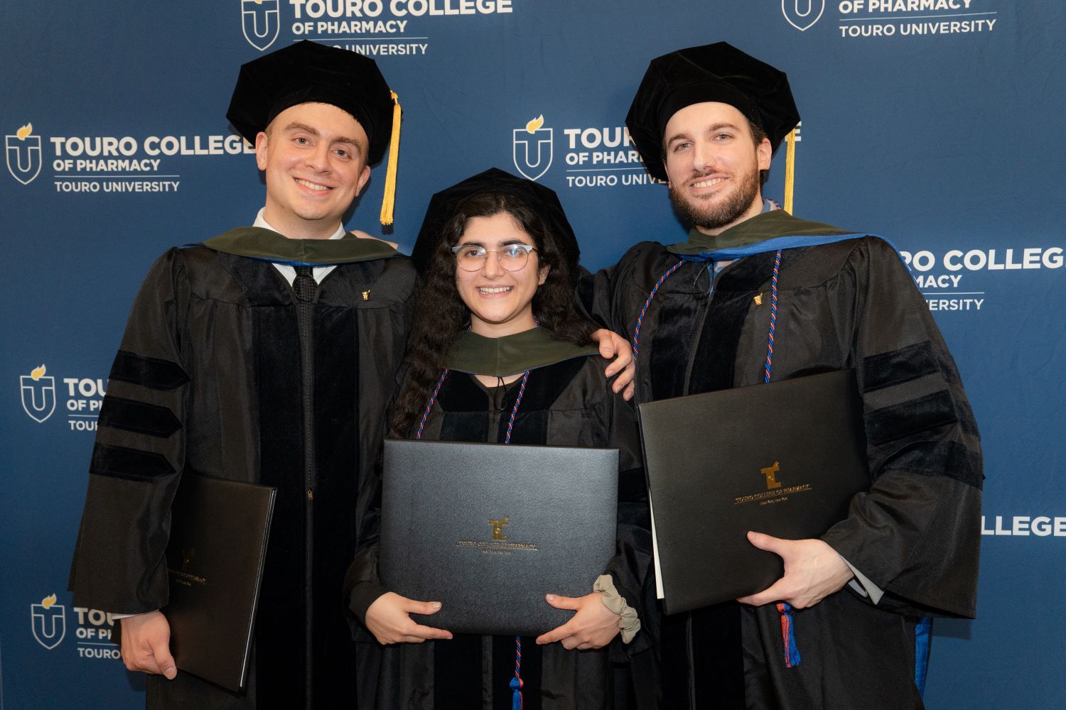 Three members of TCOP\'s graduating class hold up their diplomas.