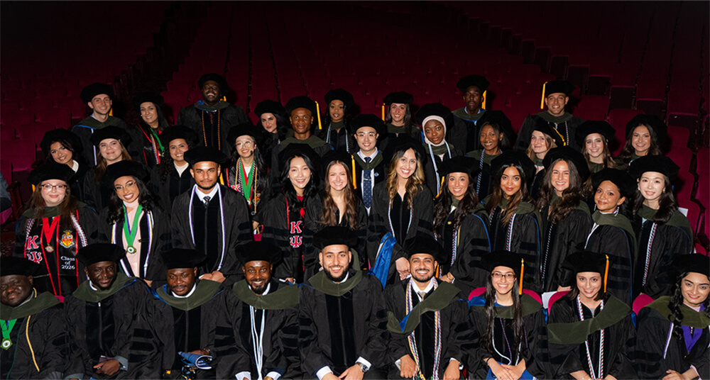 over forty men and women robed in velvet caps and gowns sitting in auditorium together in a group smiling at camera for group photo before ceremonies begin at Town Hall.