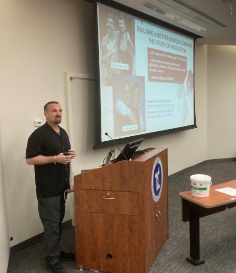 Dr. George Yancopoulos at podium speaking to pharmacy students about his company in lecture hall.