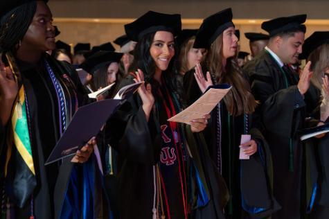 Graduates standing and reciting their pharmacy oath, woman in center looking up and smiling at camera