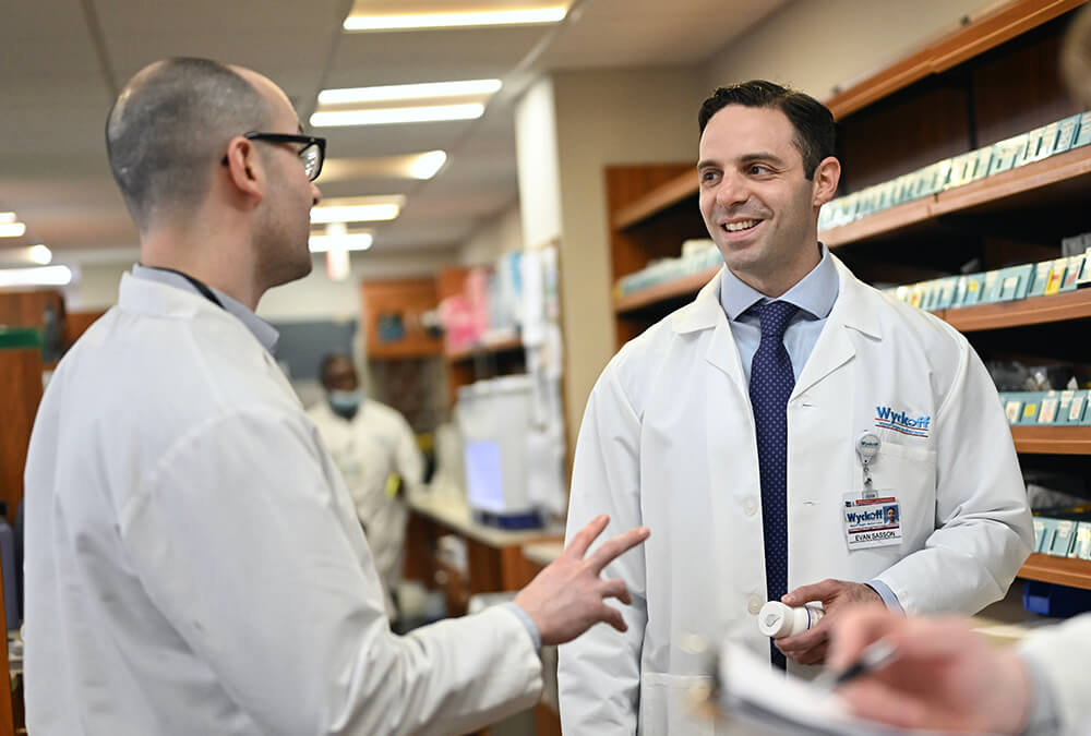 Pharmacist Evan Sasson holding a bottle of pills and talking to a colleague at Wyckoff Heights Medical Center