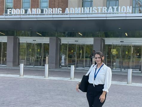 pharmacy student standing outdoors in plaza in front of large government building 
