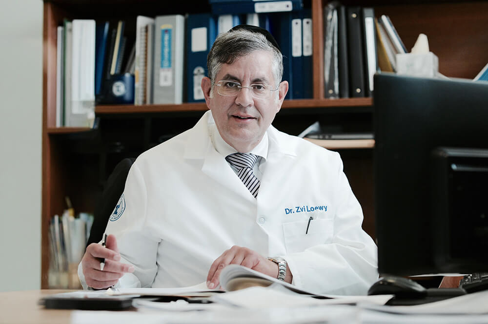 Dr. Zvi Loewy sitting at his desk in his office in front of a bookcase with books