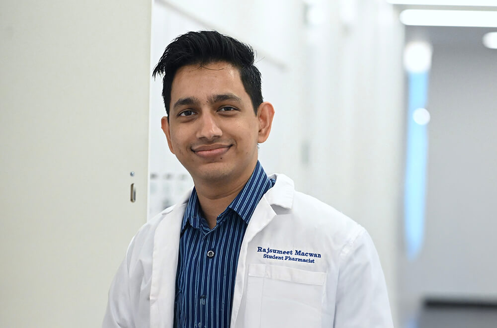 Rajsumeet Macwan in white coat, standing next to white lockers in hallway