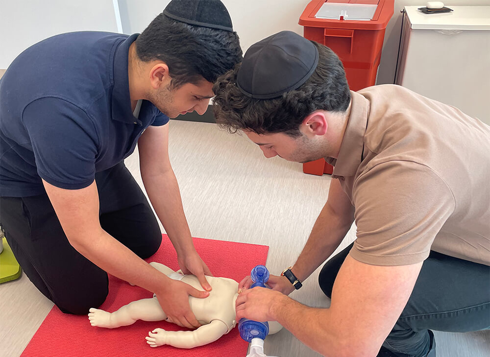 two male college students leaning over a baby mannequin practicing CPR